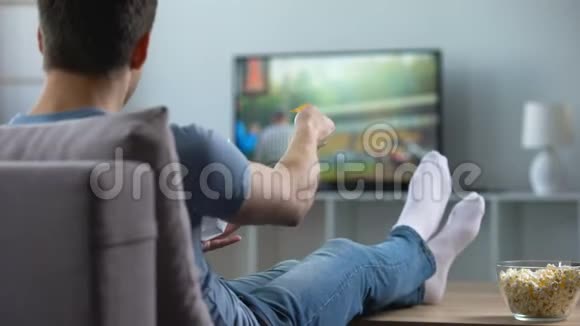 男子看美式足球在沙发上吃零食回家周末休闲视频的预览图