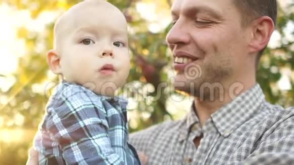 快乐的年轻父亲在秋天的公园里拥抱他两岁的儿子欢笑的男人父亲节近照视频的预览图
