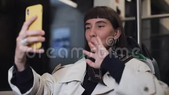 年轻的微笑女子在乘坐公共交通工具时有一个视频电话她挥动手与朋友交谈视频的预览图