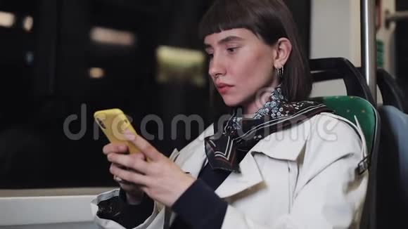 坐在公共交通工具里望着窗外的年轻沮丧的女人她手里拿着智能手机视频的预览图