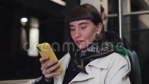 年轻的时髦女人坐在公共交通工具上的智能手机上聊天Stedicam射击年轻女子收到好消息视频的预览图