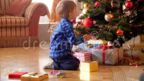小男孩坐在客厅的地板上用棍子和球装饰圣诞树的4K镜头家庭视频的预览图