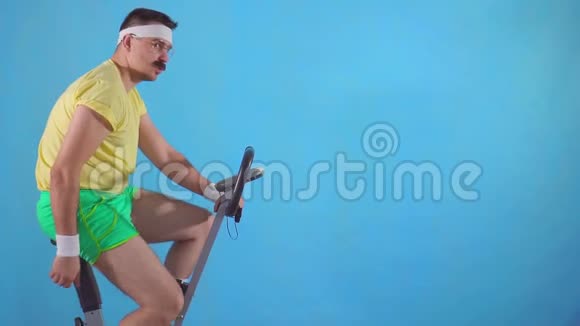 这位80的滑稽男子在蓝色背景下骑着运动自行车手里长着胡子他的拇指向上缓缓移动视频的预览图