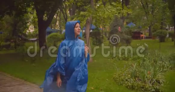 穿着蓝色雨衣在公园里散步的白种人年轻女性的特写镜头视频的预览图