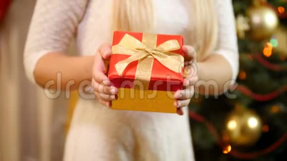 客厅里一位年轻女子站在圣诞树旁手里拿着红色圣诞礼盒视频的预览图