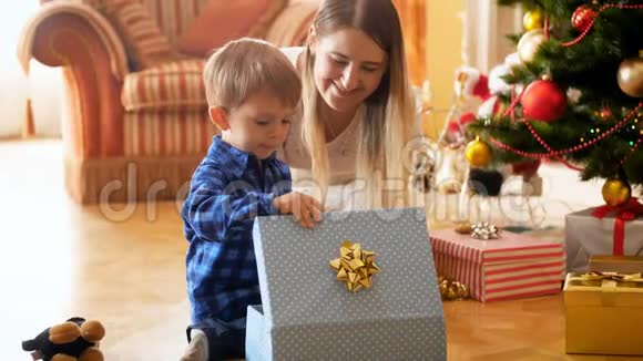 小男孩坐在圣诞树旁边把玩具装在五颜六色的盒子里家庭捐赠和视频的预览图