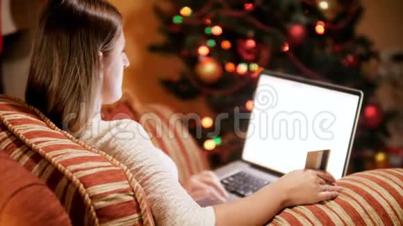 4k视频年轻女子在客厅的扶手椅上放松旁边是发光的圣诞树手持信用卡视频的预览图