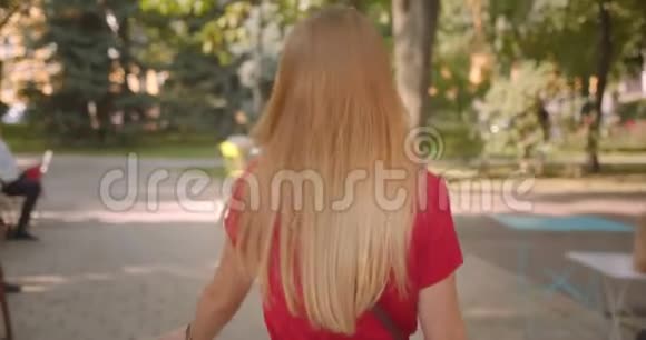 近景后景照片年轻的金发碧眼的美丽女性走在公园的咖啡馆里转过身来视频的预览图