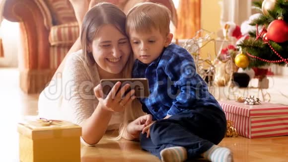 快乐微笑的4k视频快乐躺在圣诞树下使用智能手机家庭有美好的时光视频的预览图
