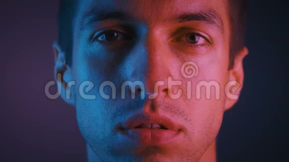 一幅英俊的年轻人在霓虹灯中用严肃而自信的表情看着相机的肖像视频的预览图