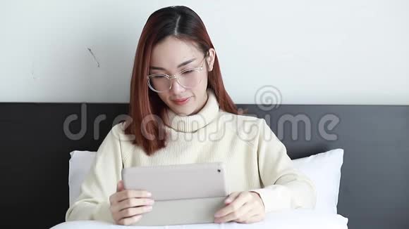 十几岁的亚洲女孩在家里躺在床上玩智能平板电脑上的网络游戏视频的预览图
