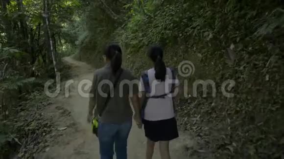 母亲和女儿的后景是在沿着小溪徒步旅行的小径上手拉手散步的视频的预览图