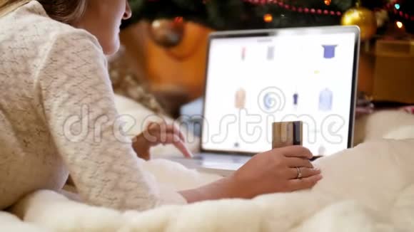 特写4k镜头年轻女子手持信用卡躺在电脑旁的地板上浏览网上商店视频的预览图