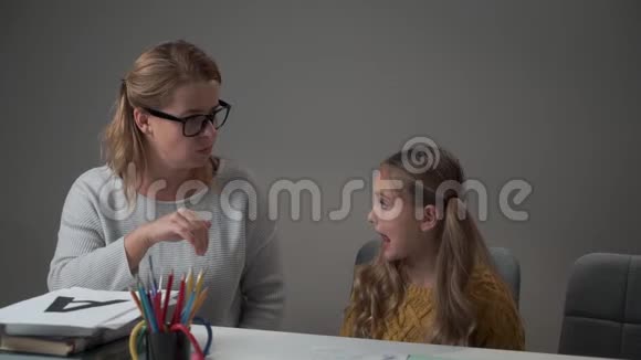一位女性高加索家庭教师的眼镜和小女孩学习字母的肖像智慧青年教师视频的预览图