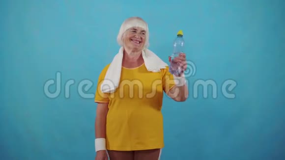 积极积极的运动老太太水瓶在蓝色背景上竖起大拇指视频的预览图
