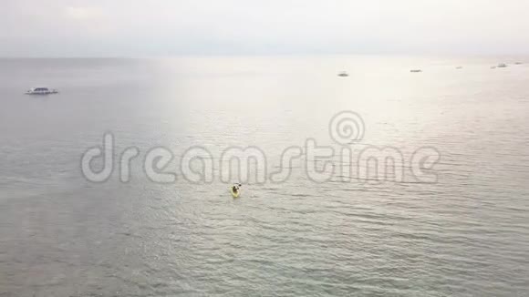 一位年轻的皮划艇运动员在平静的海洋中划着一艘黄色的小船的空中景色视频的预览图