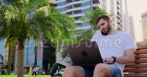 夏天一个穿着白色t恤手提电脑的男人在长凳上打电话视频的预览图