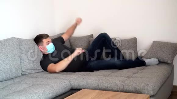 被隔离的戴着医用口罩的冠状病毒携带者睡觉后躺在沙发上自我隔离大流行视频的预览图
