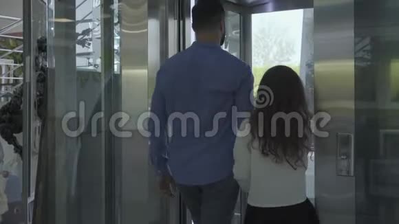 自信的白人男人和可爱的小女孩进入现代玻璃升降机爸爸按下按钮电梯就要开了视频的预览图