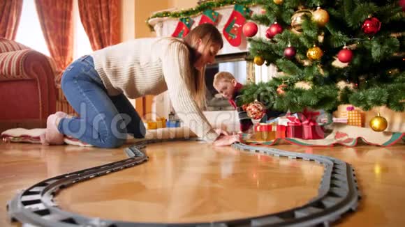 4k镜头快乐微笑的家庭和小男孩在圣诞树周围为小玩具火车修建铁路儿童视频的预览图