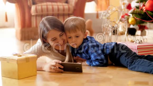 小男孩和年轻母亲躺在客厅的地板上在智能手机上看动画片的4K镜头家庭视频的预览图