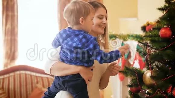 客厅里圣诞树上挂着小男孩和小儿子的快乐微笑的年轻妈妈的4k镜头视频的预览图