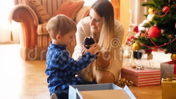 可爱的小男孩和他的母亲在礼物盒里包装玩具在圣诞节送礼物的视频家庭捐赠和视频的预览图