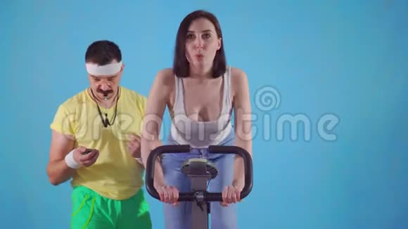 80带胡子和眼镜的滑稽男教练正在检查一名年轻女子的运动自行车视频的预览图