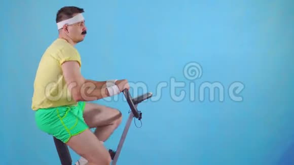 这位80的滑稽男子在蓝色背景下骑着运动自行车手里长着胡子视频的预览图