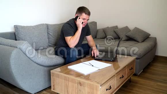 检疫冠状病毒COVID19距离工作年轻的商人用智能手机说话坐着笔记本电脑办公室主任视频的预览图