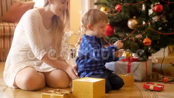 4k镜头快乐微笑的小男孩坐在圣诞树下打开圣诞礼物和礼物视频的预览图
