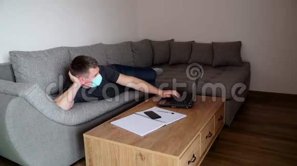 戴着医疗面具的商人很累在工作场所躺着工作检疫冠状病毒COVID19远程视频的预览图