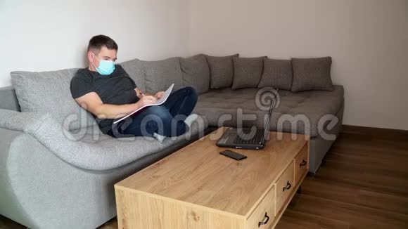 一个戴着医疗面具的商人坐在沙发上远程工作与家庭有关的远程工作视频的预览图