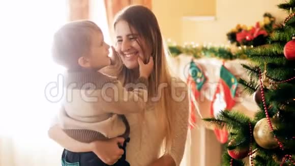 快乐的年轻母亲在客厅的圣诞树旁边抱着她的小儿子的4K视频家庭成员视频的预览图