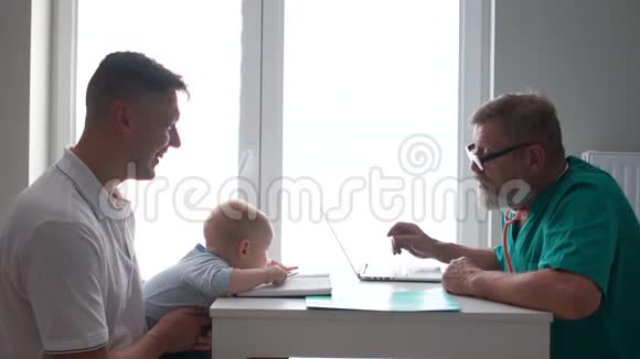 父亲和一个小儿子在儿科医生约会医生把病人抱怨写在笔记本电脑上男性视频的预览图