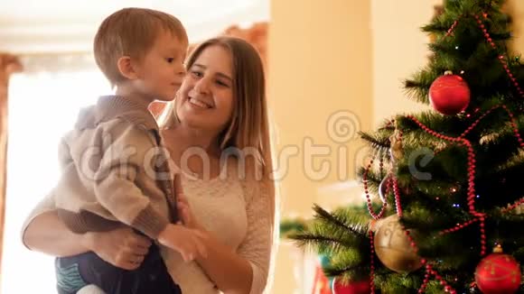 快乐的母亲和她的小儿子站着看房子里腐烂的圣诞树的4K镜头家庭视频的预览图