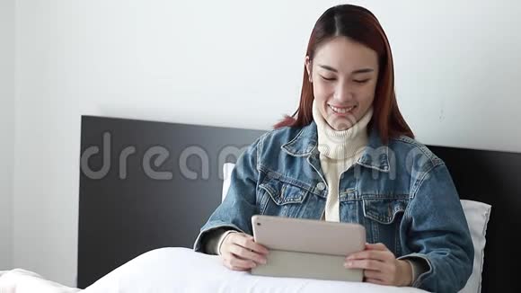 快乐的女人早上在电脑平板电脑上在线看视频新闻亚洲女孩在卧室里视频的预览图