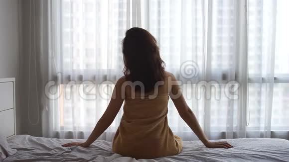 女人穿着毛巾在卧室的床上伸展身体低亮度视频的预览图