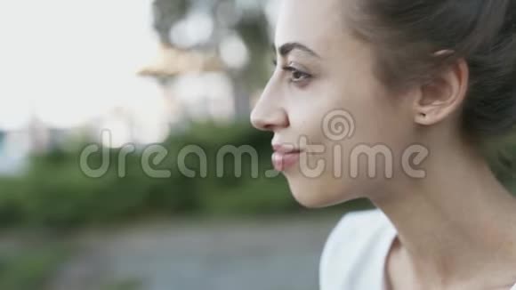白色t恤的迷人年轻女人的特写侧景夏天晚上女人坐在公园里视频的预览图
