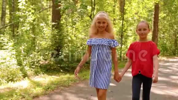 两个美丽的微笑女孩散步牵手夏天公园视频的预览图