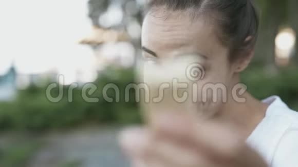 穿着白色t恤的身材苗条的年轻女子夏天晚上坐在公园里吃华夫饼视频的预览图