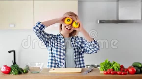 快乐迷人的年轻女孩在烹调健康食品时手拿新鲜的黄胡椒在眼睛上跳舞视频的预览图