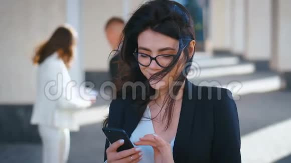 一位年轻漂亮的商务女性她带着智能手机发短信一边在外面工作一边微笑视频的预览图
