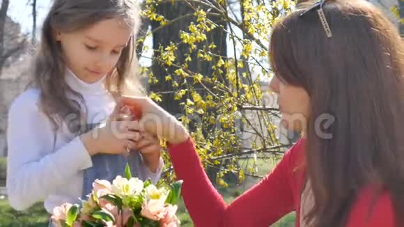 金发的小女儿从花束里拿出一朵花放进她牛仔装的口袋里快乐的母亲视频的预览图