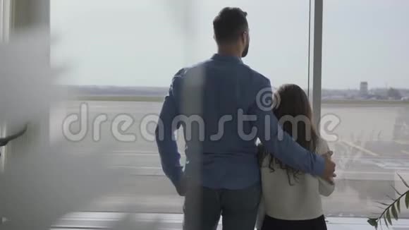 从后面可以看到成年白人男子和小女孩站在机场看窗户女儿在等视频的预览图