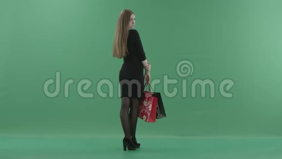 美丽快乐的女人穿着小黑裙子摆着购物袋她站在演播室的后面视频的预览图