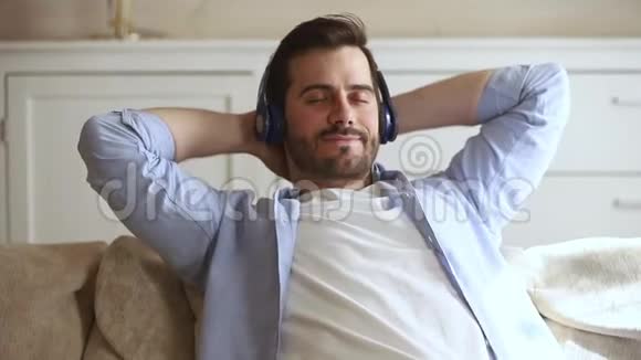 躺在沙发上的年轻人通过耳机听音乐视频的预览图