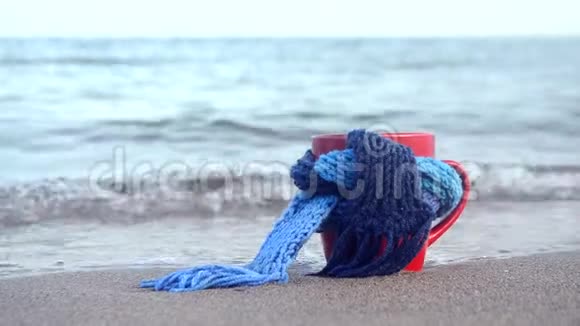 带着蓝色针织围巾的咖啡红马克杯站在沙滩上视频的预览图