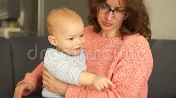 一位母亲和蹒跚学步的孩子坐在家里的沙发上母亲节的亲密肖像妈妈和她的孩子拥抱视频的预览图