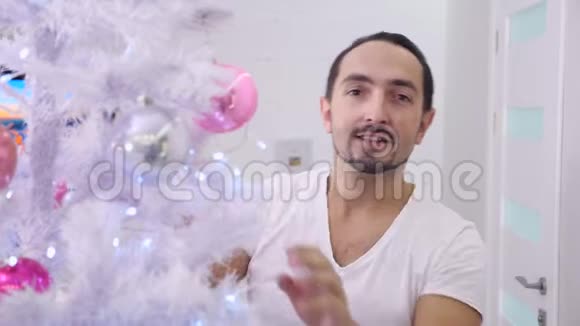 在皮贾马的男人把最后一个球挂在圣诞树上看着眯着眼睛视频的预览图